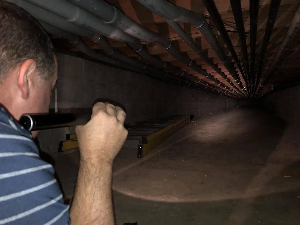 Perry inspecting floor joists and plumbing in a crawlspace